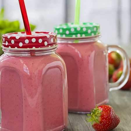 Strawberry smoothies in a glass bottle, mint leaves and whole strawberry berries on a gray wooden background. The concept of diet, fitness and healthy eating. Soft focus. Square.の写真素材