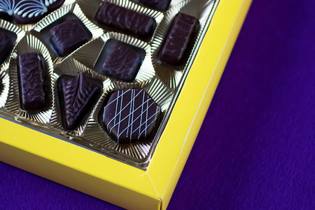 Assorted chocolates in yellow box on  purple background. Soft focus.