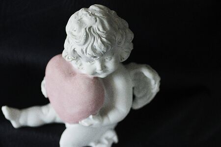White angel with a pink heart in hands on a black background. Soft focus.の写真素材