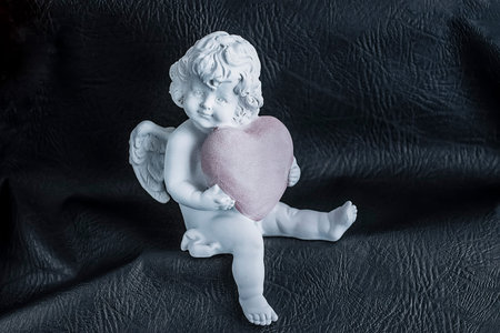 Angel with a pink heart in hands on a black background. Soft focus.