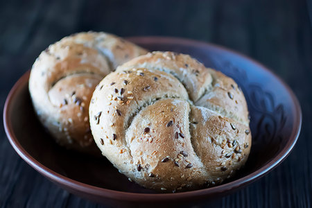 Two multigrain buns with sesame seeds and flaxseed on a brown plate. Soft focus.