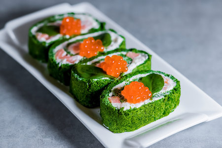 Spinach biscuit roll with cottage cheese, salted salmon and red caviar on a white rectangular plate...