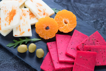 Assorted cheeses with herbs, olives, walnuts and fruits on a black slate board. Soft focus.の写真素材