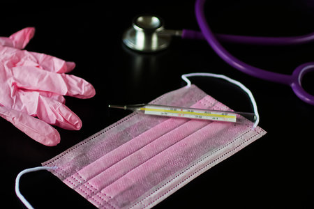SOFT FOCUS. Coronavirus concept. Medical mask, pink medical gloves, stethoscope, computer and thermometer on a black background.の写真素材