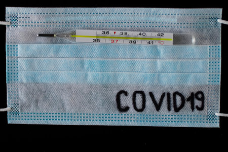Blue disposable medical mask and thermometer on black background. Coronavirus concept.