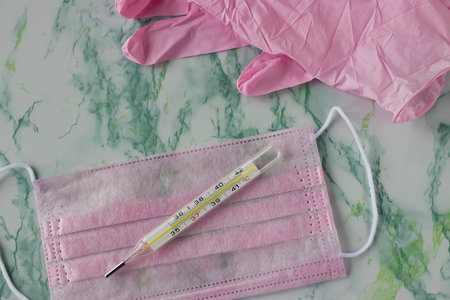 Pink medical mask, pink medical gloves and a thermometer. Coronavirus concept.