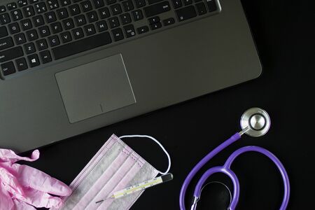 Coronavirus concept. Medical mask, pink medical gloves, stethoscope, computer and thermometer on a black background.の写真素材