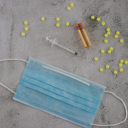 Yellow pills, syringe and vaccine bottle on a gray cement background. World vaccination concept....