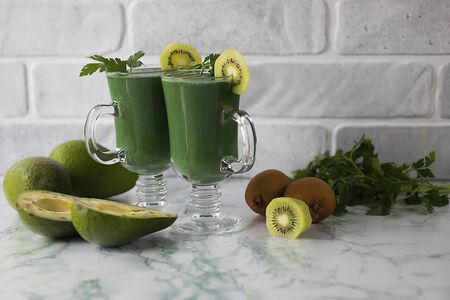Green smoothie made of greens, kiwi, avocado, apple and spirulina in glass glasses on a marble table. Superfood concept. Soft focus.の写真素材