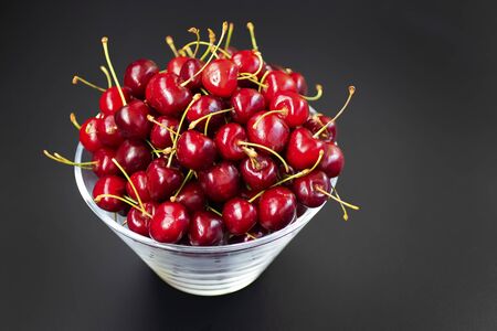 Ripe organic sweet cherries in a glass bowl on a black table.  Soft focus.の写真素材