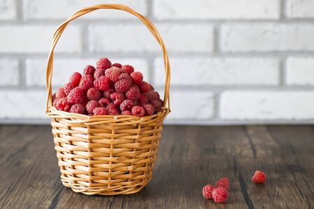 Ripe organic raspberries in brown basket on brown wooden background. Soft focus.の写真素材
