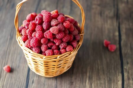 Ripe organic raspberries in brown basket on brown wooden background. Soft focus.の写真素材