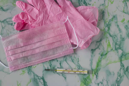 Pink medical mask, pink medical gloves and thermometer on light background. Soft focus.の写真素材