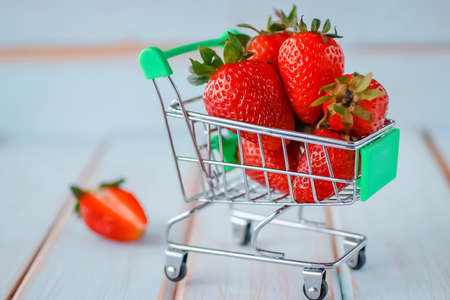 Fresh strawberries in a supermarket trolley on wooden background. Soft focus.の写真素材