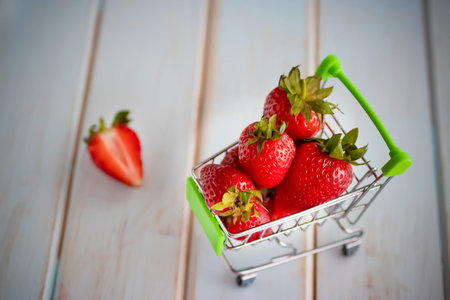 Fresh strawberries in a supermarket trolley on wooden background. Soft focus.