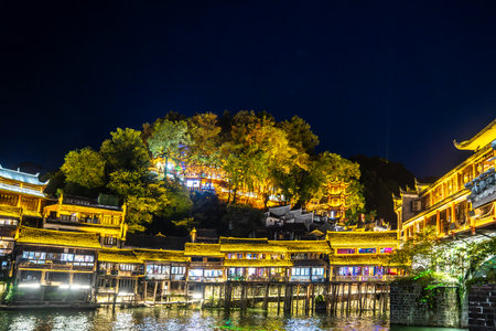 The image shows the ancient town of Fenghuang in Xiangxi, Hunan at night, illuminated and reflected in the river, full of festive atmosphereの写真素材