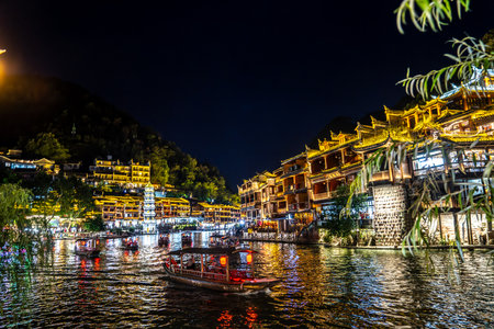 The image shows the ancient town of Fenghuang in Xiangxi, Hunan at night, illuminated and reflected in the river, full of festive atmosphereの写真素材