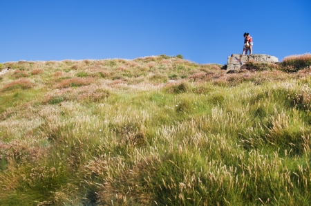 two people hugging on a rock under a blue skyの写真素材
