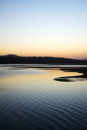 Sea and sandy beach backlit by the ocean sunset.の写真素材