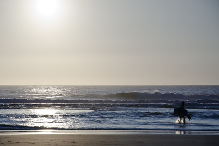 surfer walking into the abstract waves at sunset.の写真素材