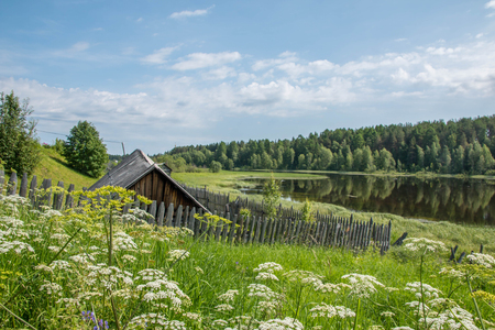 north Russian village Isady. Summer day, Emca river, old cottages on the shore, old wooden bridge and clouds reflections.の写真素材