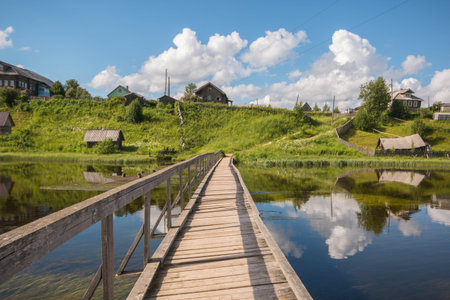 north Russian village Isady. Summer day, Emca river, old cottages on the shore, old wooden bridge and clouds reflectionsの写真素材