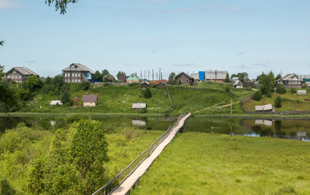 north Russian village Isady. Summer day, Emca river, old cottages on the shore, old wooden bridge and clouds reflectionsの写真素材