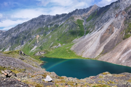 A small rainbow over the lake in the mountains. Subalpine zone in the Eastern Sayan Mountainsの写真素材