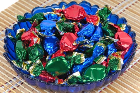 Chocolate candy with wrappers of different colors in the glass blue dishの写真素材