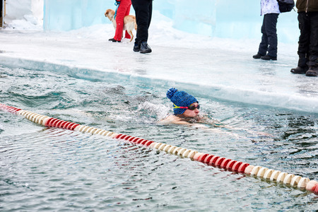 SAHYURTA, IRKUTSK REGION, RUSSIA - March 11.2017: Cup of Baikal. Winter Swimming Competitions. Woman swims in cold water in knitted hat with pomponのeditorial素材