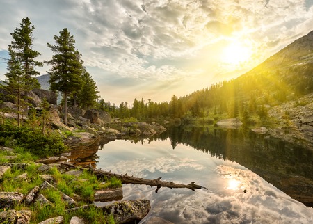 Summer morning over little lake. Sun rays shine between clouds. Ergaki Nature Park. Krasnoyarsk region Russiaの写真素材