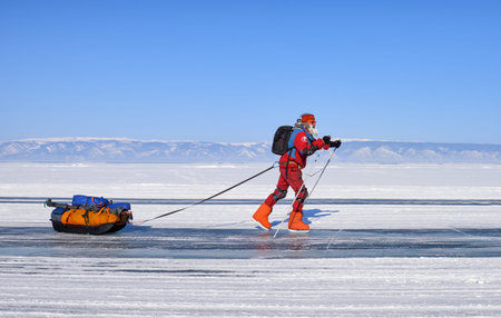 LAKE BAIKAL, IRKUTSK REGION, RUSSIA - March 08, 2017: Mature man on skates is actively moving along icy road. Behind investigator, a sleigh with an expeditionary load is attached to researcher, necessary for autonomous travel in conditions of low temperatのeditorial素材