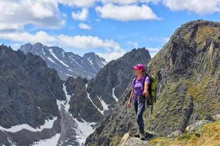 Tourist exploring beauty of mountain peaks. A woman with a backpack is standing on edge of topの写真素材