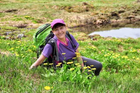 Smiling woman sits on blooming alpine lawn. Summer travel along mountain tundra in Eastern Siberia. Leisure activities in midst of natureの写真素材