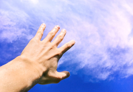 Hand against the sky and clouds, the hand reaching for the sky