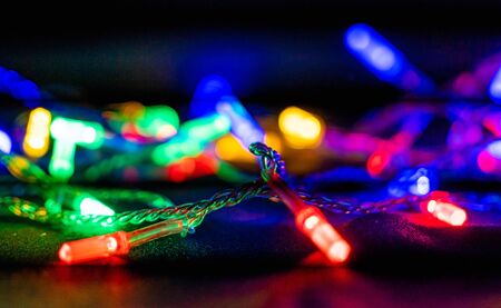 Multicolored garland with glowing lights on black background. Blurred background, bright colored light bulbs, lights, the light from the garland. Soft focus.の写真素材