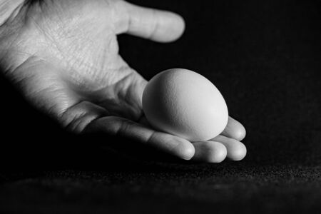 Egg in hand closeup on black background with space for text. Concept of life and health.Black and white photography art, soft focus and hard light.の写真素材