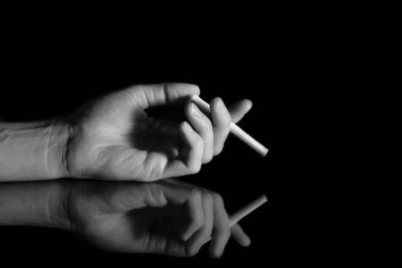 Cigarette in hand on black background with reflection. The concept on the subject of health and Smokingの写真素材