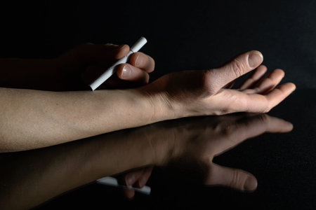 Cigarette in hand on black background with reflection. The concept on the subject of health and...
