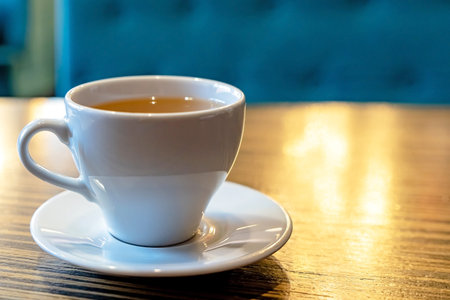 A white Cup of tea on a wooden table in a cafe close-up. Blurred background and with space for text.
