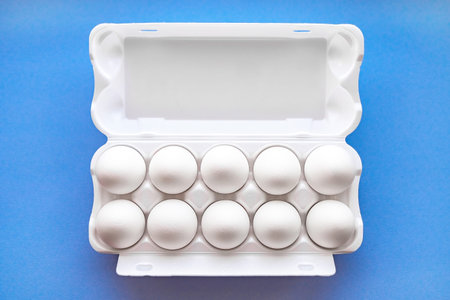 White eggs in a package on a blue background close-up view from above. Soft focus.