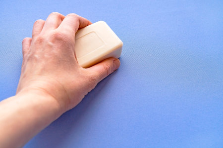 Soap for hand washing. Bar of soap in hand close-up on a blue background. Space for text.