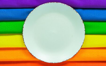 White plate on a rainbow flag LGBT flag of six colors for design. Design of the dining table for the LGBT community. Gay pride rainbow.Rainbow tablecloth for lunch.の写真素材