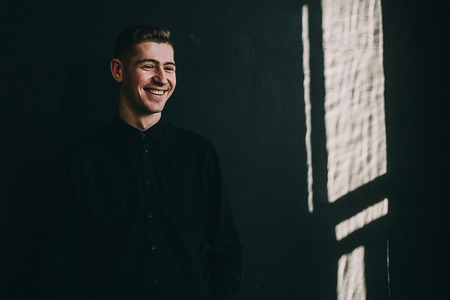 Portrait of happy hipster man smiling up near black wall.の写真素材