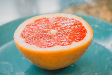 A half of a grapefruit laying on blue plate closeup on grey backgroundの写真素材