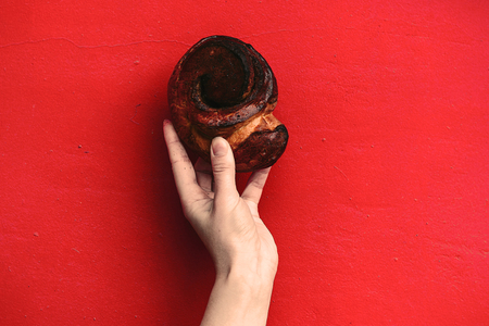 hand holding a cinnamon bun isolated on a red vintage wall backgroundの写真素材