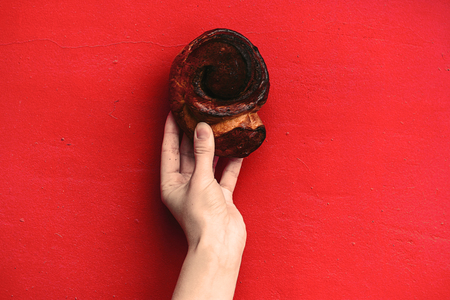 hand holding a cinnamon bun isolated on a red vintage wall backgroundの写真素材