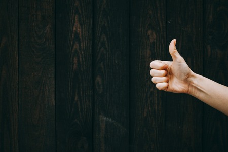 Closeup of male hand showing thumbs up sign against wooden backgroundの写真素材