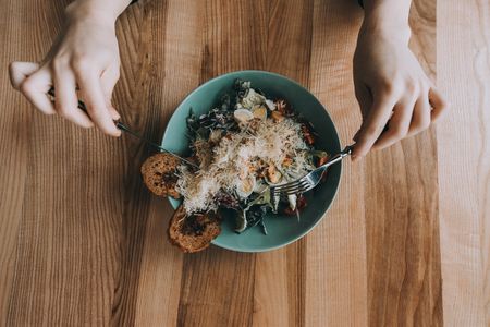 Flatlay salad with girl hands, knife and fork. Caesar salad on a wooden background. food colectionの写真素材