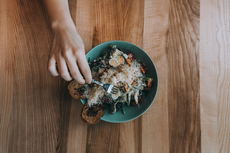 Flatlay salad with girl hands, knife and fork. Caesar salad on a wooden background. food colectionの写真素材